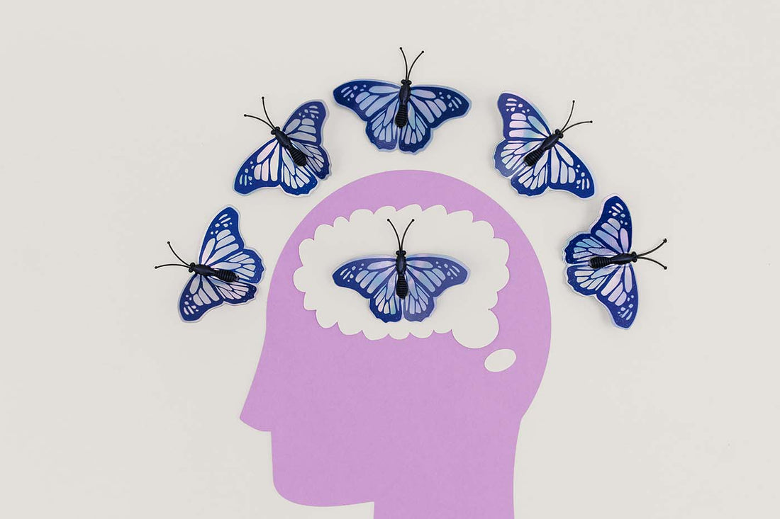 Illustration of a purple human head silhouette with butterflies flying around and inside the brain area, symbolizing thoughts, mental health, creativity, or mindfulness.