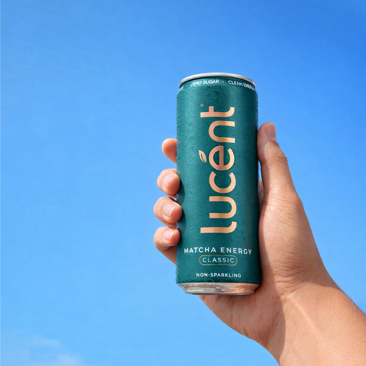 Hand holding a Lucent matcha energy drink can against a clear blue sky