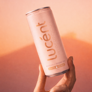 Hand holding a Lucent matcha energy drink can against a warm sunset background.