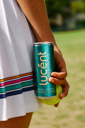 Person holding a can of Lucent before tennis in an outdoor setting
