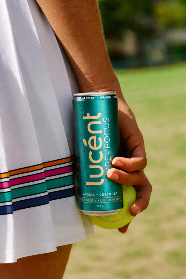 Person holding a can of Lucent before tennis in an outdoor setting